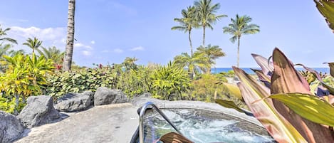 Un jacuzzi con vistas despejadas al océano, rodeado de plantas tropicales y palmeras.