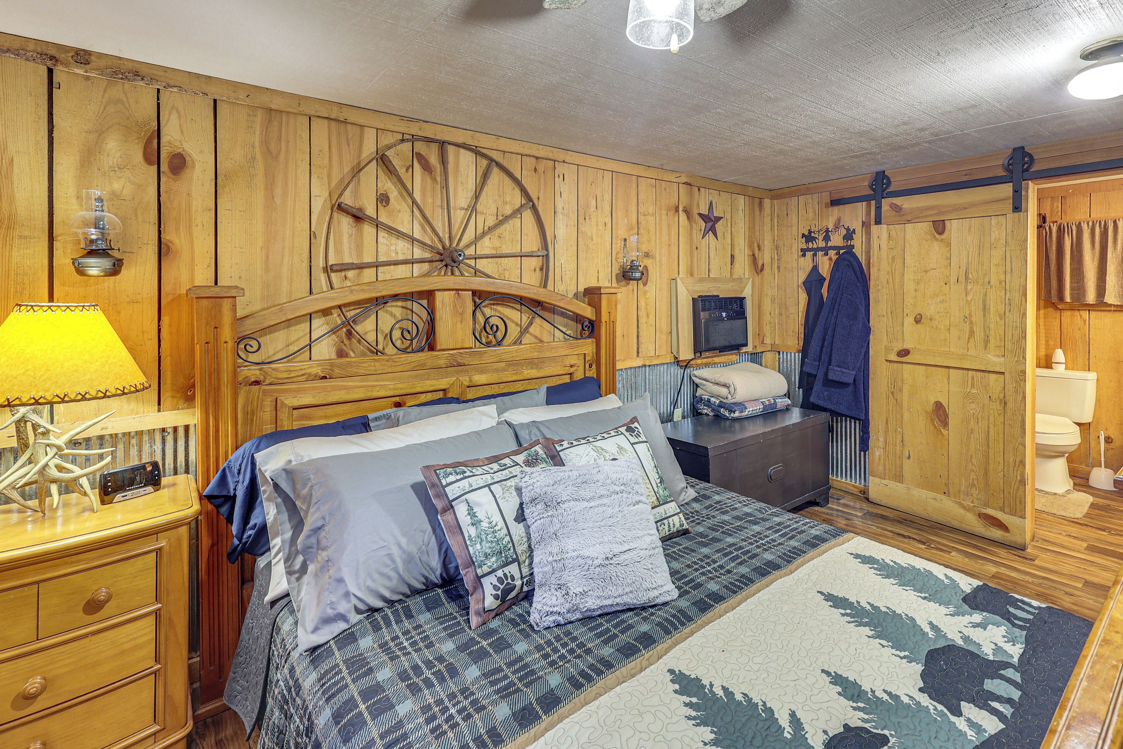 A wooden-themed bedroom with a bed, a nightstand, a lamp, a heater, a dresser, and a wardrobe.