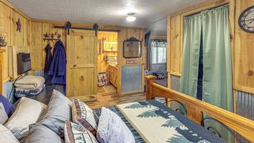 A cabin interior with a wooden floor, a sofa, a dining table, and a kitchen area.