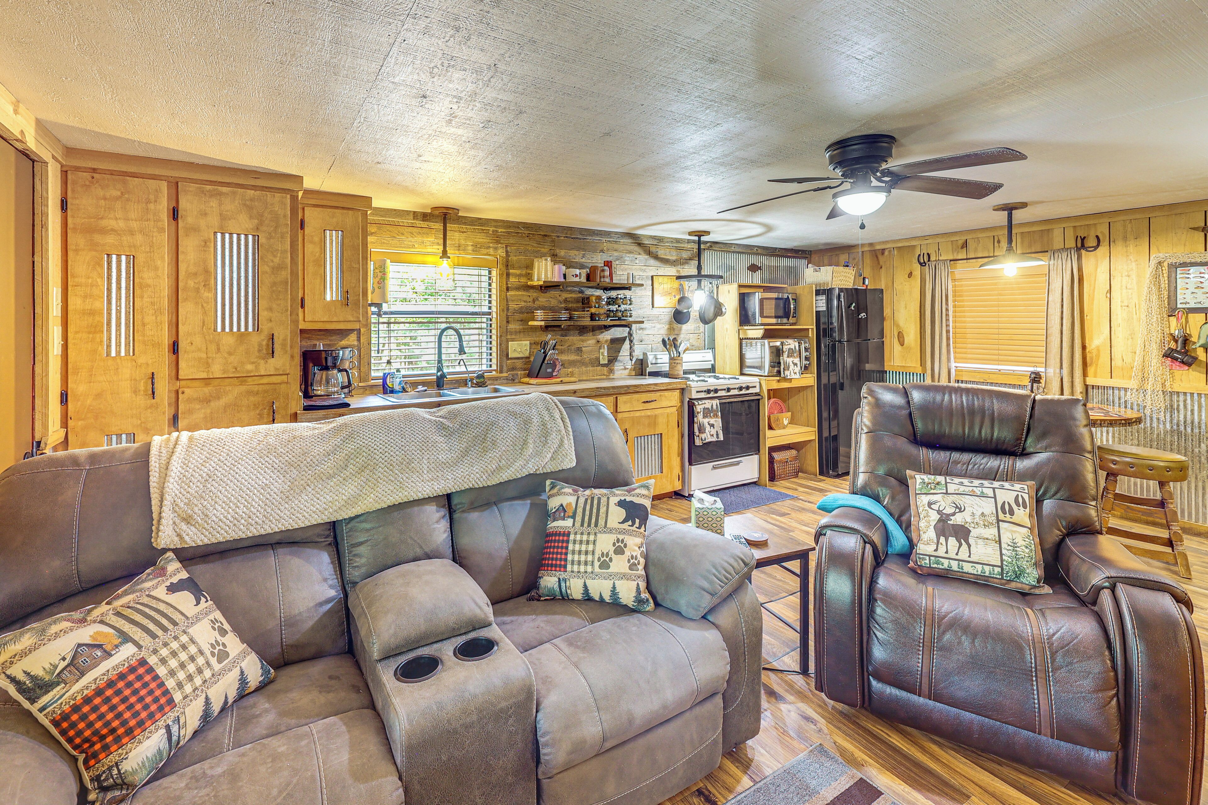 A cozy living room with a leather sofa, a dining area, and a kitchen with wooden cabinets and a ceiling fan.