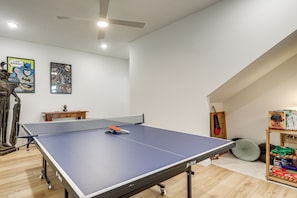 Ein Tischtennis-Tisch in einem Raum mit Deckenventilator, einem Holzbüro und einem Bücherregal.