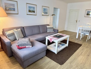 A living room with a grey sofa, a coffee table, a lamp, and framed pictures on the wall. - Strandstraße, Apartment 65 - Cozy, centrally located 2-room apartment, close to the beach, 2 balconies, (Sylt)