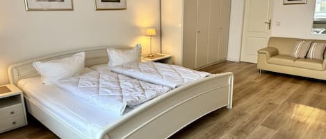A bedroom with a bed, bedside tables, a wardrobe, a sofa, and a lamp.