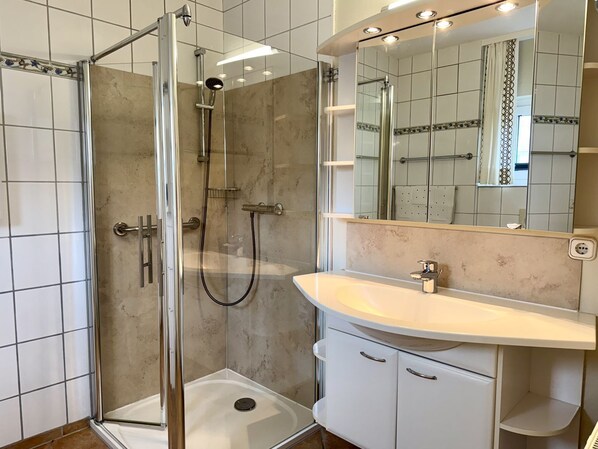 Un baño moderno con ducha envuelta en vidrio, un lavabo blanco y un espejo sobre el mueble.