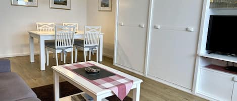 A modern living room with a dining area, a flat-screen TV, and a wardrobe.