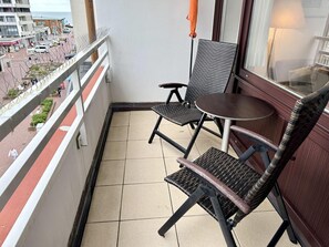 Ein Balkon mit zwei Stühlen, einem kleinen Tisch, einer Geländer und Blick auf die Straße.