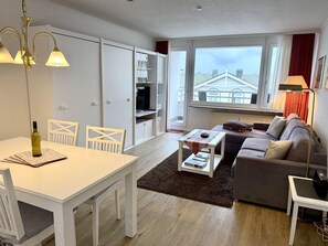 Ein modernes Wohnzimmer mit Essbereich, einer Couch, einem Couchtisch und Blick auf die Stadt durch große Fenster.