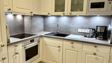 A modern kitchen with white cabinetry, a built-in microwave, a stove, and a coffee maker.