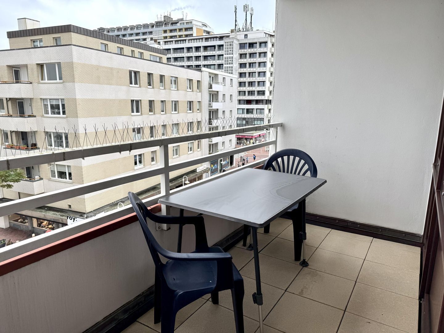 Un balcon avec une table et des chaises, donnant sur un paysage urbain composé de nombreux bâtiments.