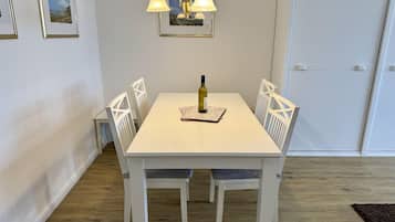A dining area with a white table, four chairs, a chandelier, and framed pictures on the wall.