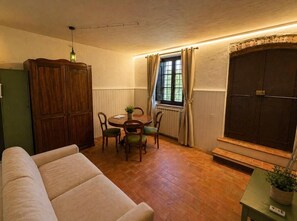 A cozy living room with a sofa, a dining table with chairs, a wooden cabinet, and a window with curtains.