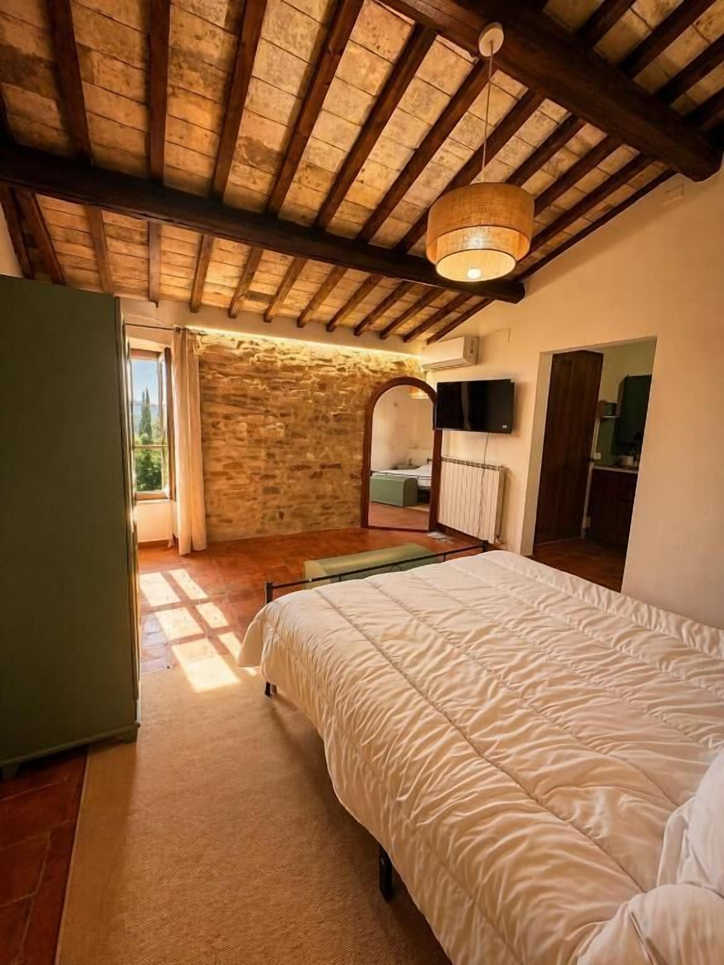 A bedroom with a bed, a stone wall, a wooden ceiling, and a television.