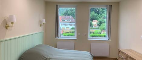 A bedroom with a bed, a dresser, two windows with curtains, and wall-mounted lights.
