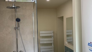 Uma casa de banho moderna com chuveiro envidraçado, pia branca e porta-toalhas.