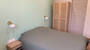 Quarto com cama, mesa de cabeceira, luminária na parede, guarda-roupa e uma porta.