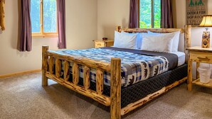 A room with a wooden bed, two windows with curtains, a bedside table, and a wall decoration. - Adventure Bay | Dock, Kayaks, Firepit & Game Room (Friendship)