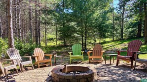 A fire pit surrounded by Adirondack chairs in a forested area. - Adventure Bay | Dock, Kayaks, Firepit & Game Room (Friendship)