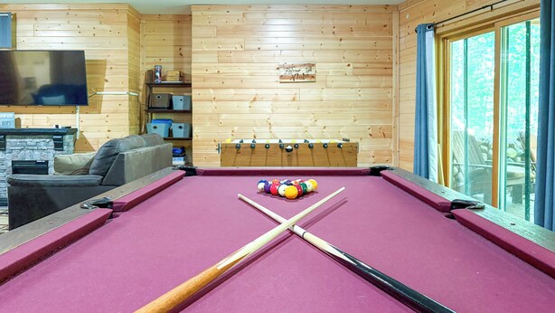 A pool table with pool cues and balls, a television, a sofa, and a window with curtains. - Adventure Bay | Dock, Kayaks, Firepit & Game Room (Friendship)