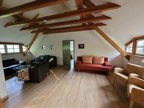 A loft-style living space with exposed wooden beams, a red sofa, a black leather couch, and a small table. - Kollhof Rügen Lauterbach - Kollhof Rügen - Pure relaxation in absolute tranquility in (Putbus)
