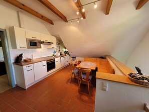 A kitchen with white cabinets, a microwave, and a dining area with a table and chairs. - Kollhof Rügen Lauterbach - Kollhof Rügen - Pure relaxation in absolute tranquility in (Putbus)