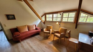 Een gezellige kamer met een rode bank, twee fauteuils, een kleine tafel en een raam met uitzicht op groen.