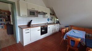Een kleine keuken met witte kastjes, een magnetron en een oven. Er is een eethoek met een tafel en stoelen.