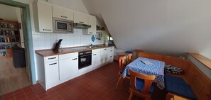 Eine kleine Küche mit weißen Schränken, einer Mikrowelle und einem Backofen. Es gibt eine Essecke mit Tisch und Stühlen.