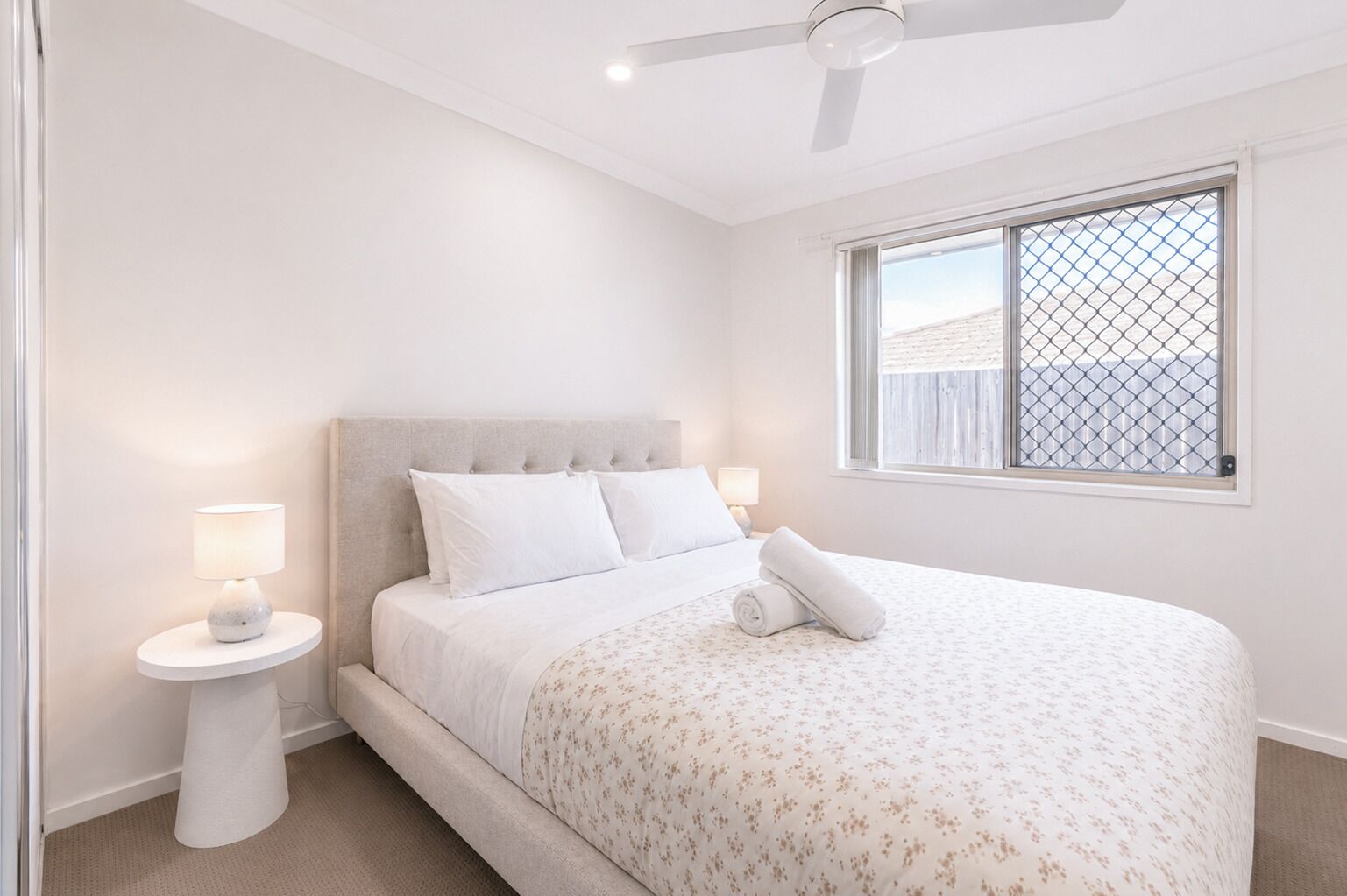 A bedroom with a bed, a nightstand, a ceiling fan, and a window with a view.