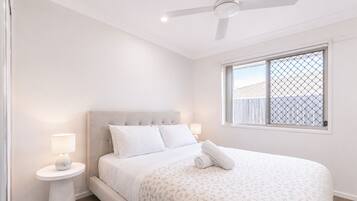 A bedroom with a bed, a nightstand, a ceiling fan, and a window with a view.
