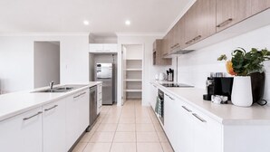 A modern kitchen with white cabinetry, a stainless steel refrigerator, and a countertop with a plant and kitchenware. - The Garden Nook | Duplex w/ Private Backyard (Waterford West)