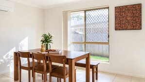 A dining area with a wooden table and chairs, a potted plant, and a window with a view of a backyard. - The Garden Nook | Duplex w/ Private Backyard (Waterford West)