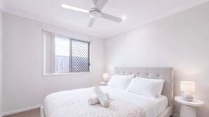 A bedroom with a bed, a ceiling fan, a window with a metal screen, and two bedside lamps. - The Garden Nook | Duplex w/ Private Backyard (Waterford West)