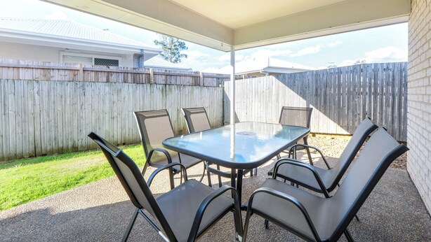 An outdoor patio with a glass table and four chairs, surrounded by a wooden fence and a grassy area. - The Garden Nook | Duplex w/ Private Backyard (Waterford West)