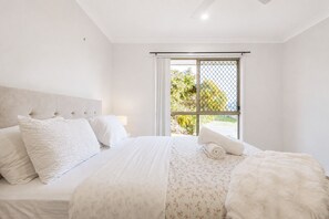 A bedroom with a bed, pillows, a blanket, and a window with a view of greenery.
