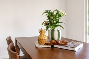 Una mesa de madera con un jarrón con forma de piña, un jarrón a rayas con flores y un libro.