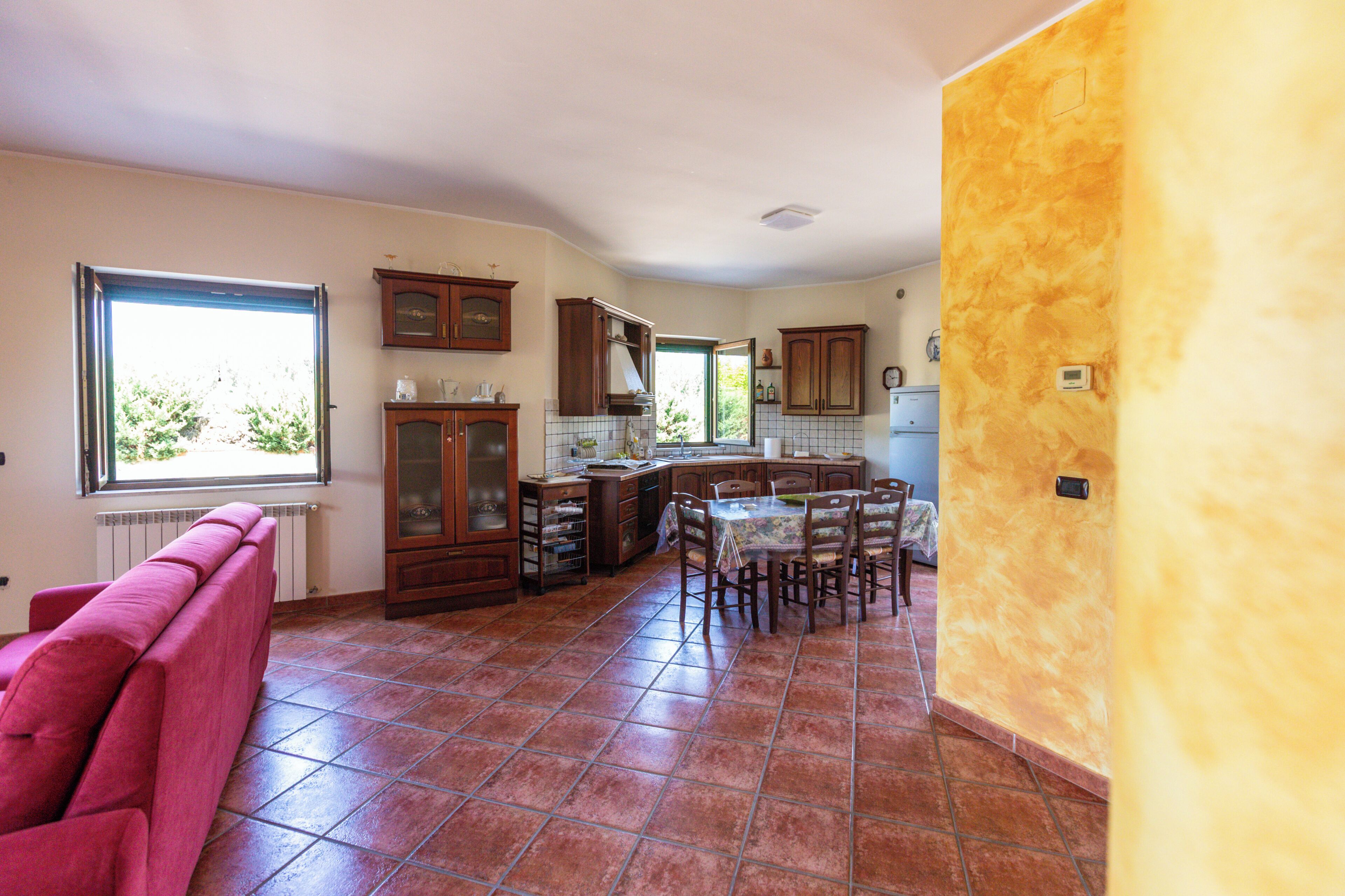 A spacious kitchen with a dining area, large windows, and a red sofa.