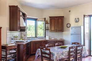 A kitchen with wooden cabinets, a dining table with chairs, a refrigerator, and a window providing natural light. - Casa Clementina - Alle porte di S. Agata dei Goti (Giardoni)