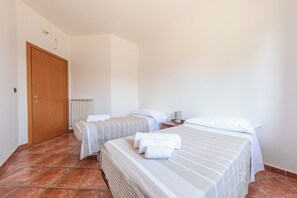 A hotel room with two beds, a wooden door, a radiator, and a tiled floor. - Casa Clementina - Alle porte di S. Agata dei Goti (Giardoni)