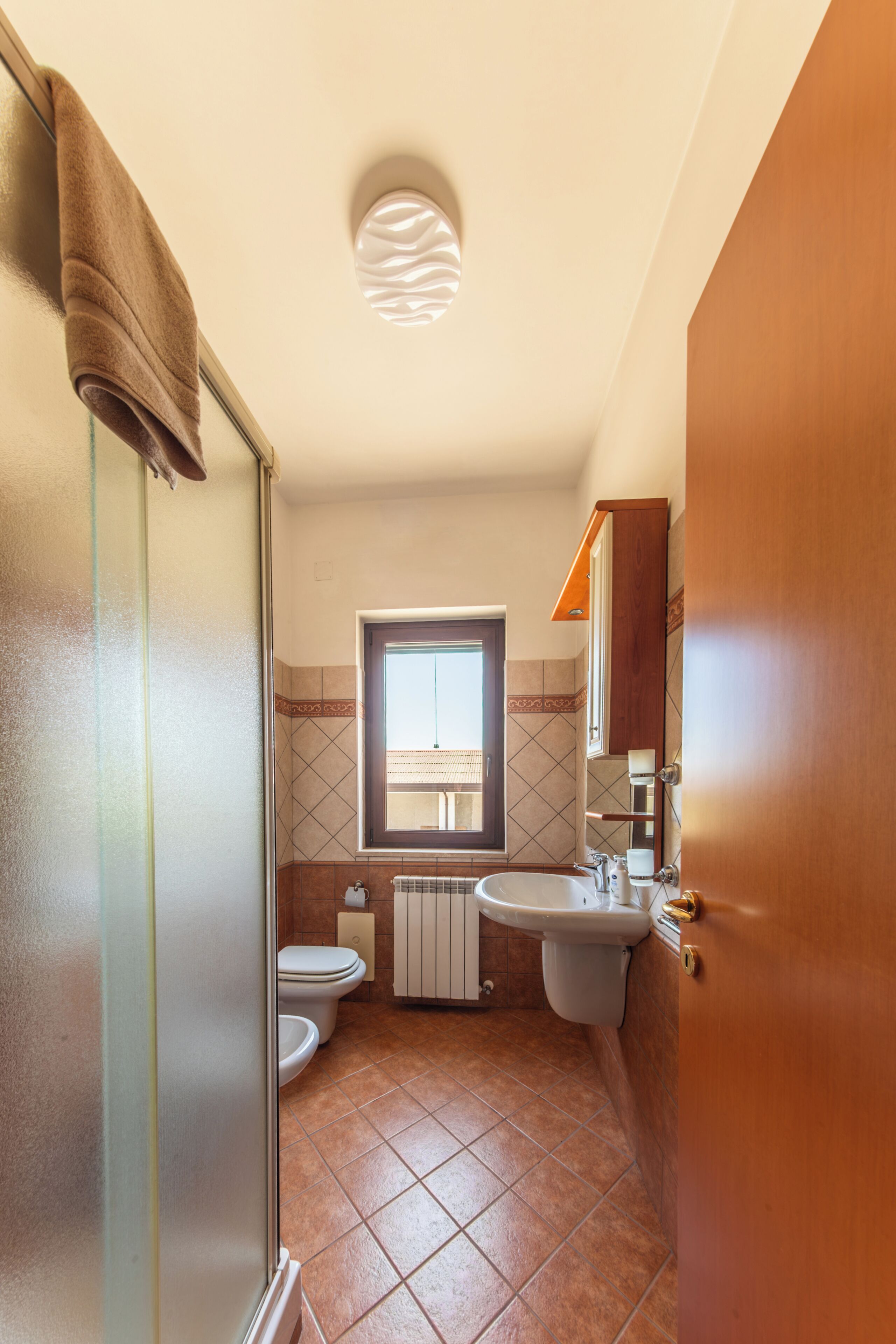 Een badkamer met douche, toilet, wastafel en een raam.