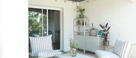 A covered patio area with a white chair, a small table, and a potted plant.