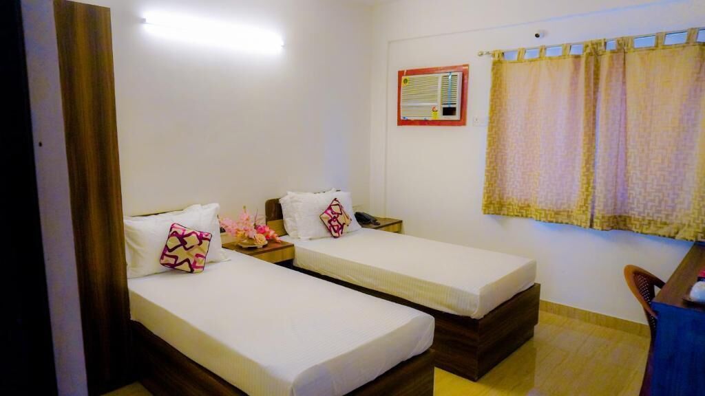Una habitación con dos camas individuales, una mesita de noche de madera, una pequeña mesa y una silla.