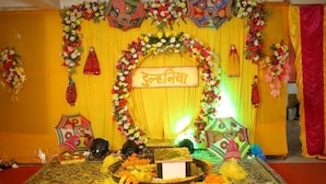 Un escenario decorado con arreglos florales, un letrero y objetos tradicionales.