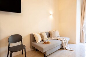 A modern living room with a sofa, a chair, a flat-screen TV mounted on the wall, and a small table with a bowl and glasses. - City Hub 5 | Elegant Historic Apartment in Central Bari  (Bari)