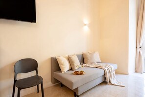 Ein modernes Wohnzimmer mit einer Couch, einem Sessel, einem flachbildfernseher an der Wand und einem kleinen Tisch mit Schale und Gläsern.