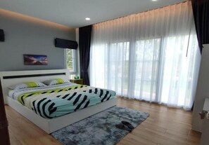 A bedroom with a bed, a rug, a window with curtains, and a wall-mounted TV.