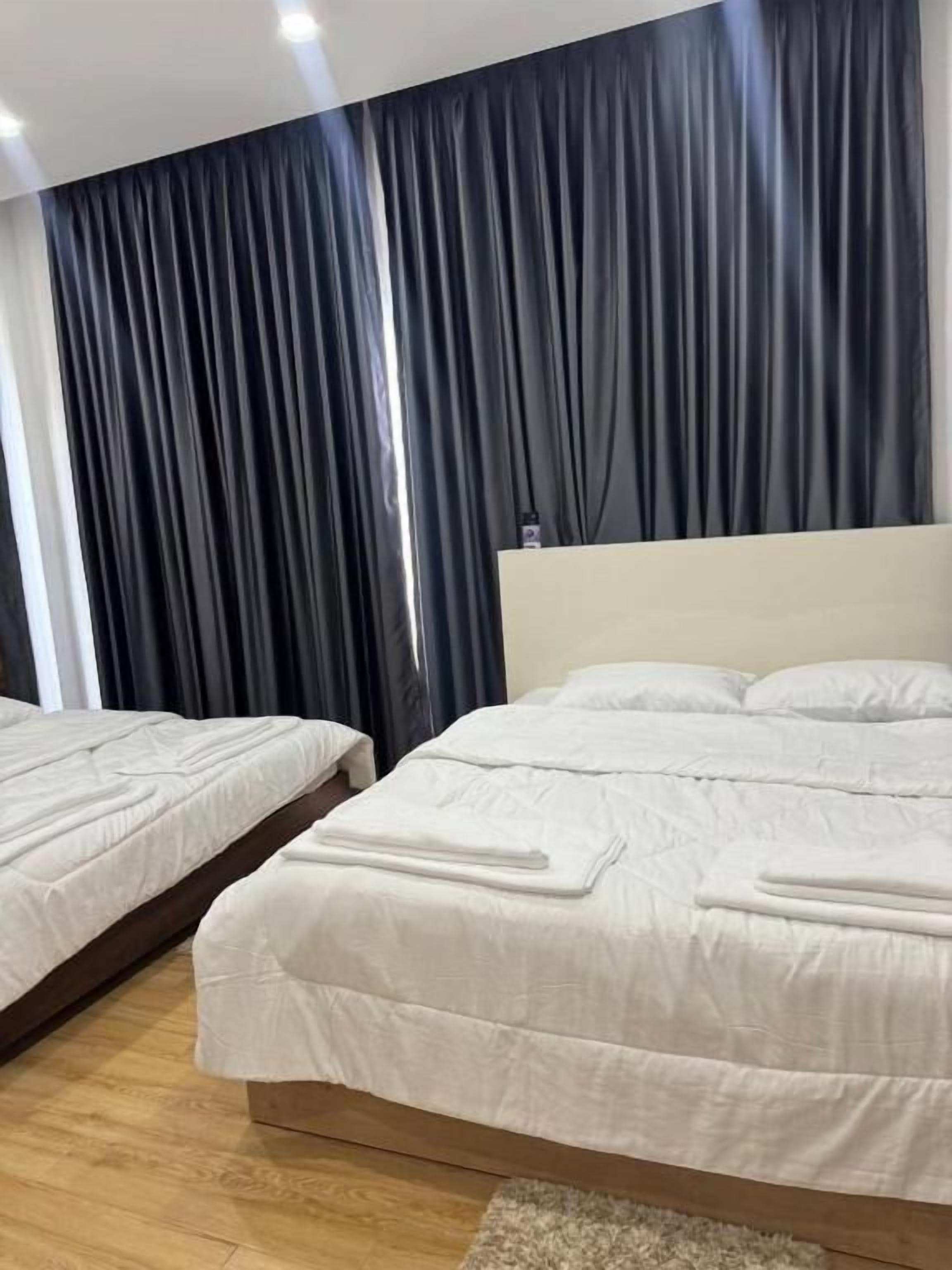 A hotel room with two beds, a large window, and a dark curtain backdrop.