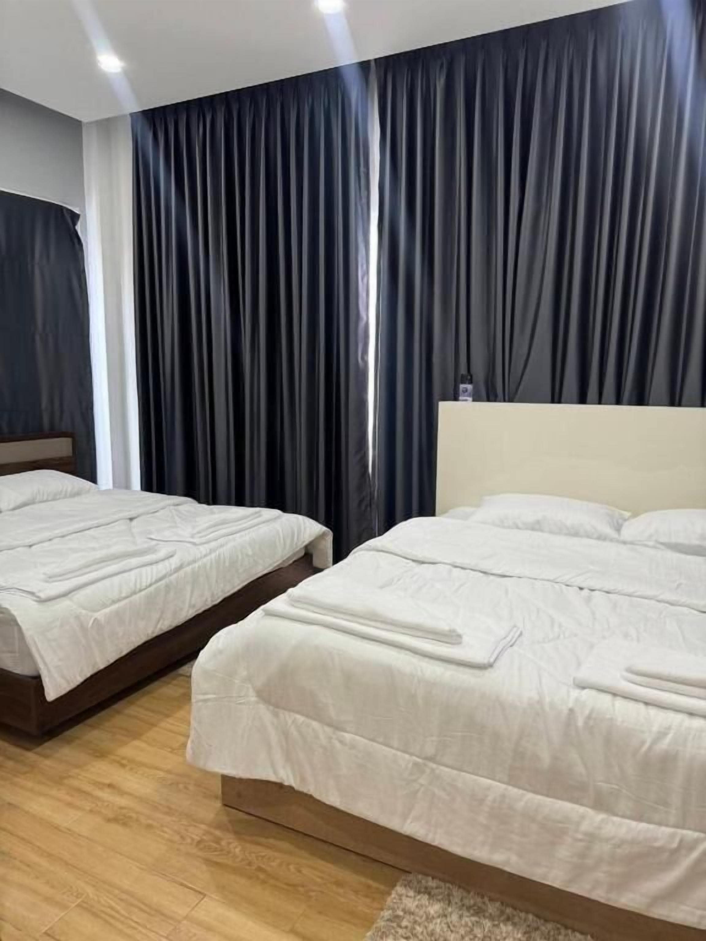 Habitación de hotel con dos camas, cortinas oscuras y suelo de madera.