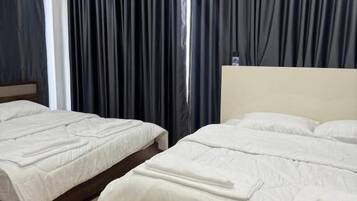 Habitación de hotel con dos camas, cortinas oscuras y suelo de madera.