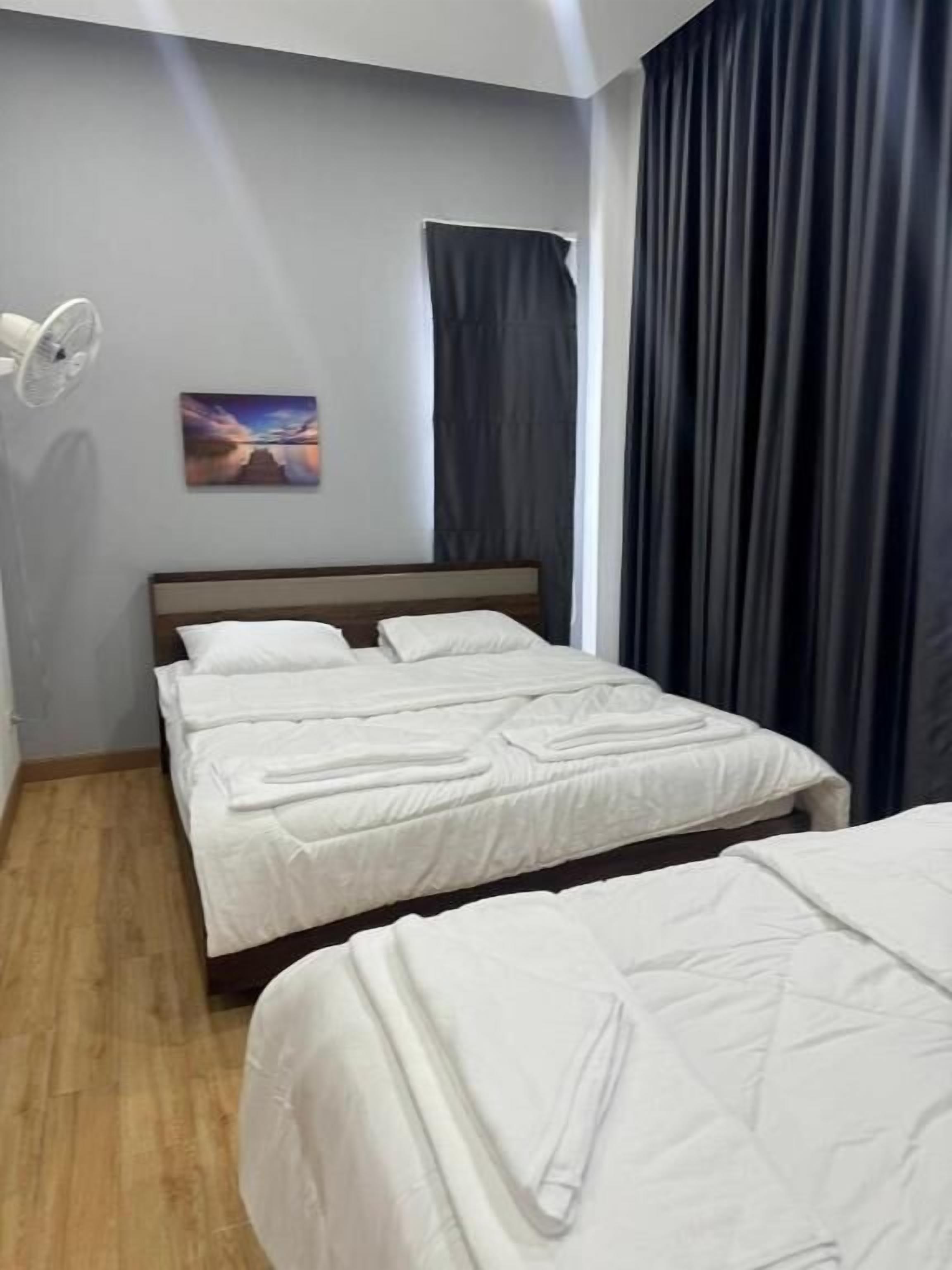 A hotel room with a bed, a bedside table, a wall-mounted fan, and a window with curtains.