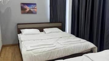 A hotel room with a bed, a bedside table, a wall-mounted fan, and a window with curtains.
